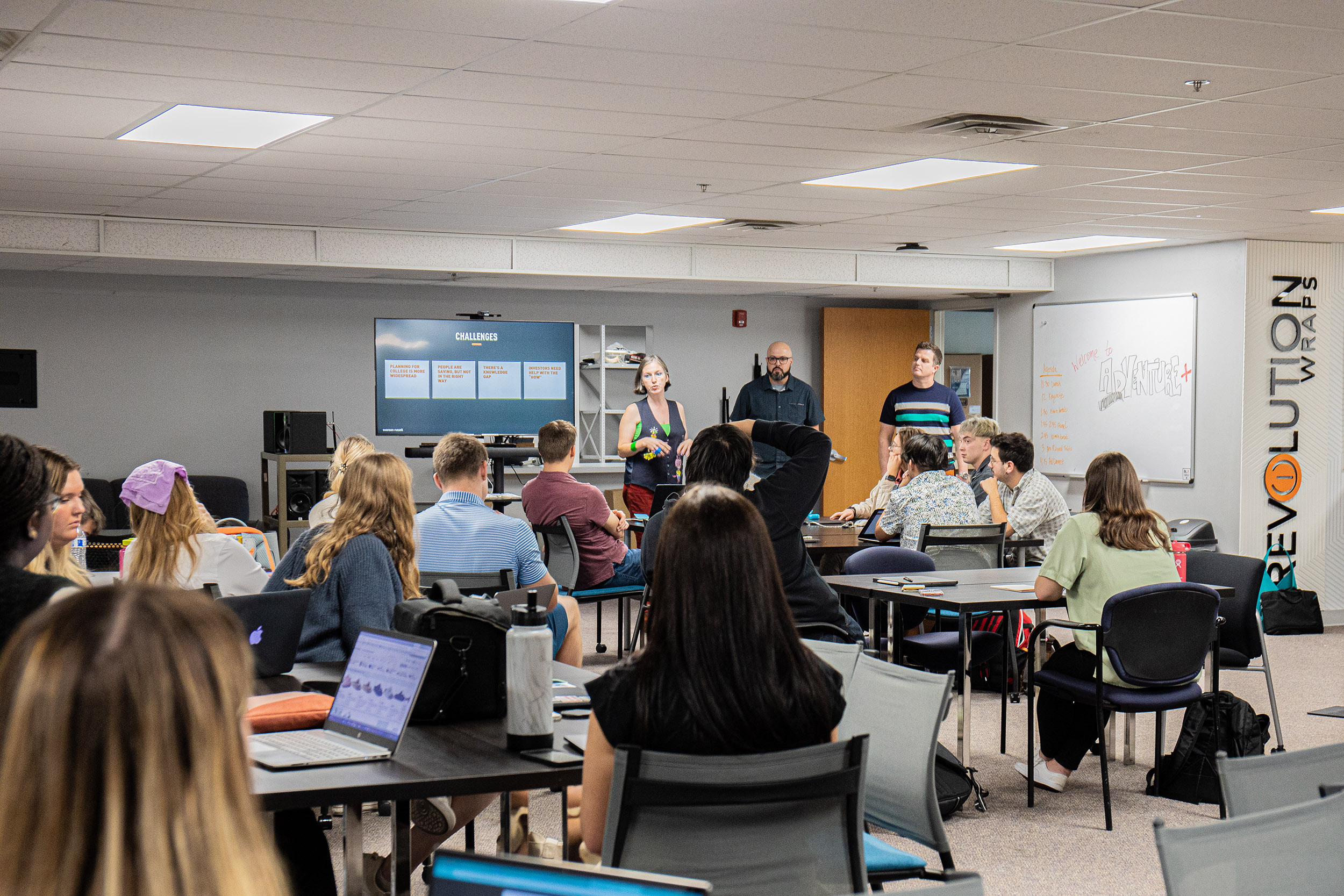 Three representatives of Swanson Russell — two men and a woman — speak to a room of a dozen-plus students in the Jacht Ad Agency.