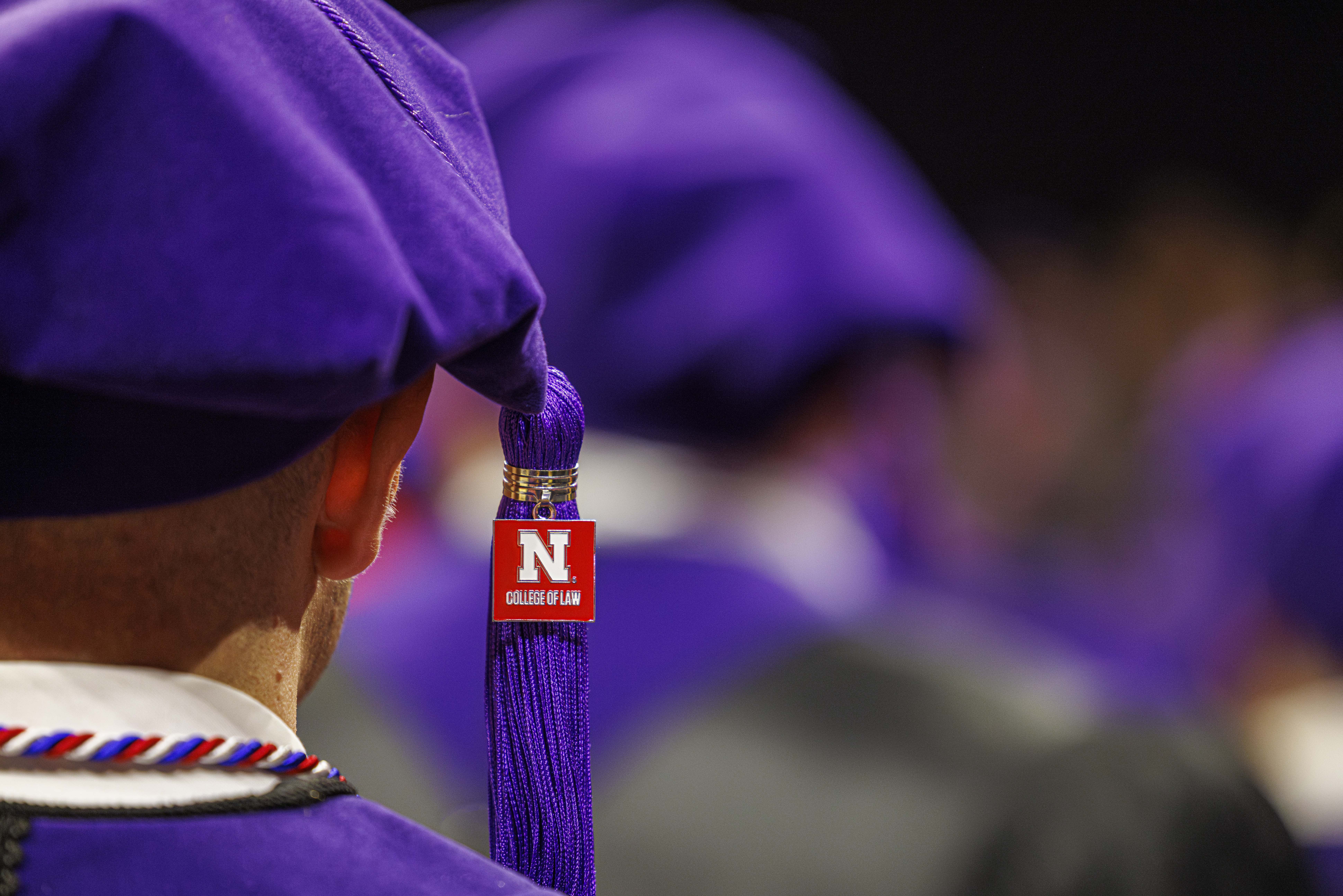 A close-up of a University of Nebraska College of Law graduate from behind. He is wearing a purple tam with a purple tassel. From the tassel hangs a red, square pendant with the Nebraska block N and the words "College of Law."