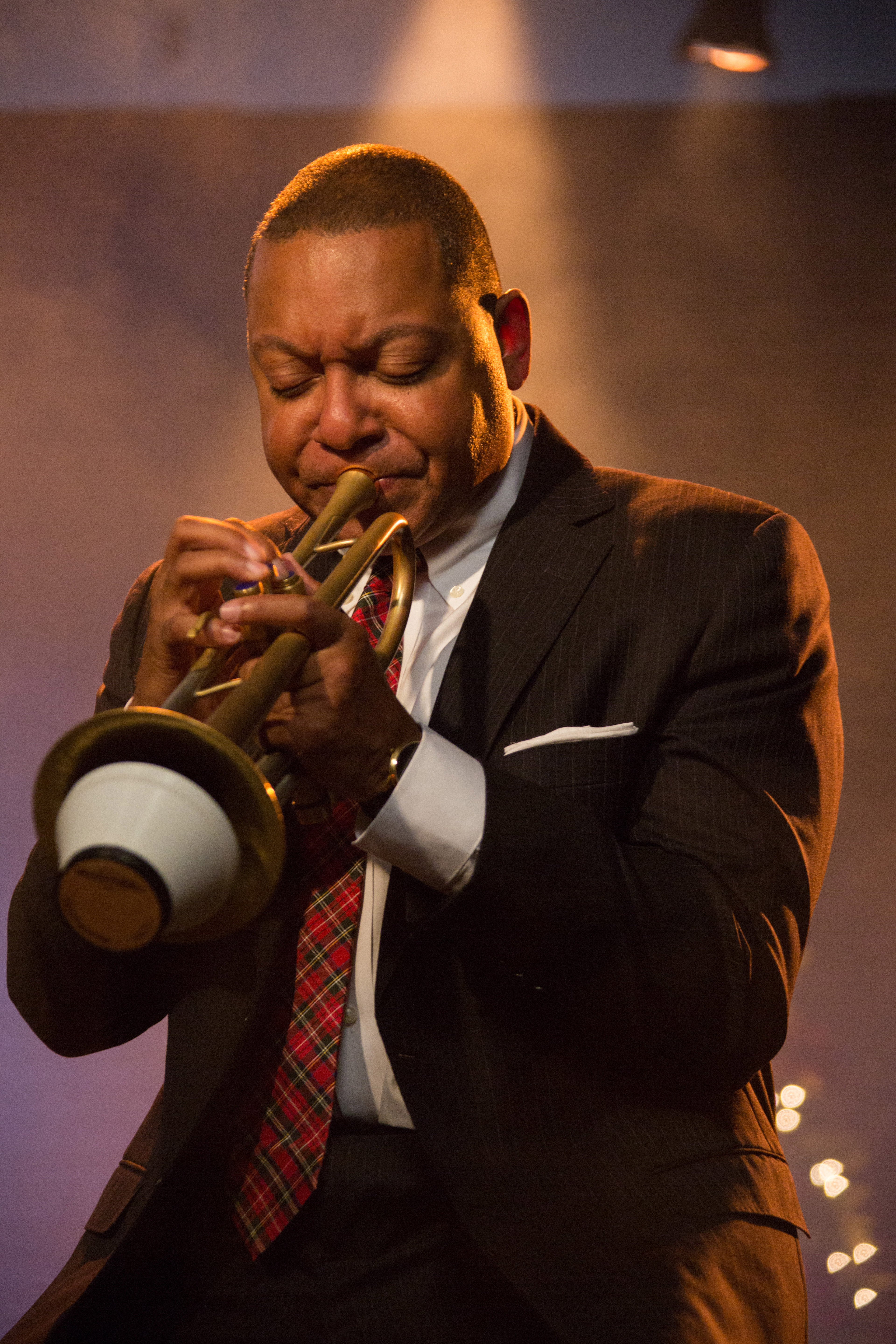 Wynton Marsalis, wearing a suit, plays a trumpet with a mute.