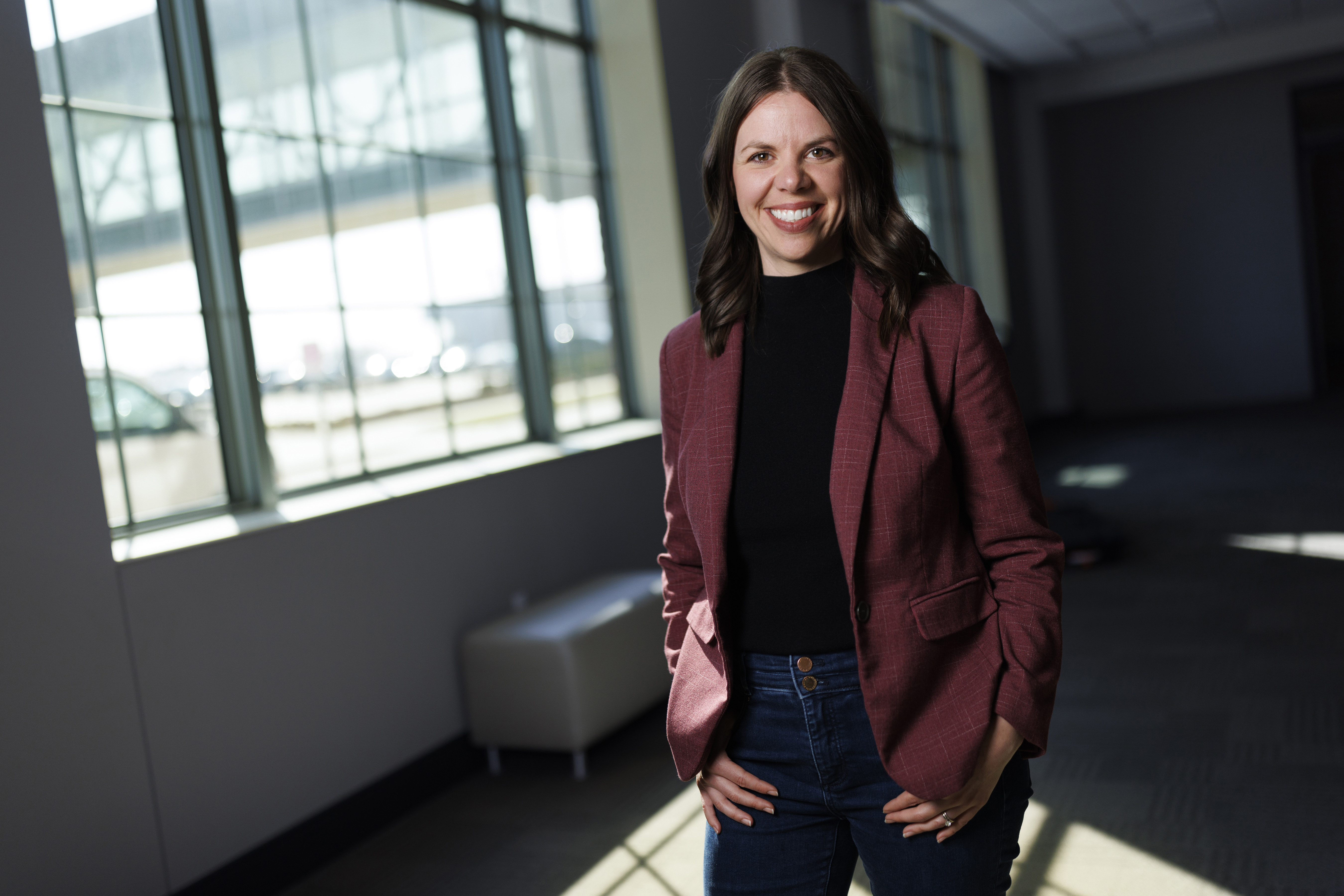 Jordyn Bader, Husker alumna and cofounder of Marble Technologies, smiles as she stands next to a window in a shadowy corridor.
