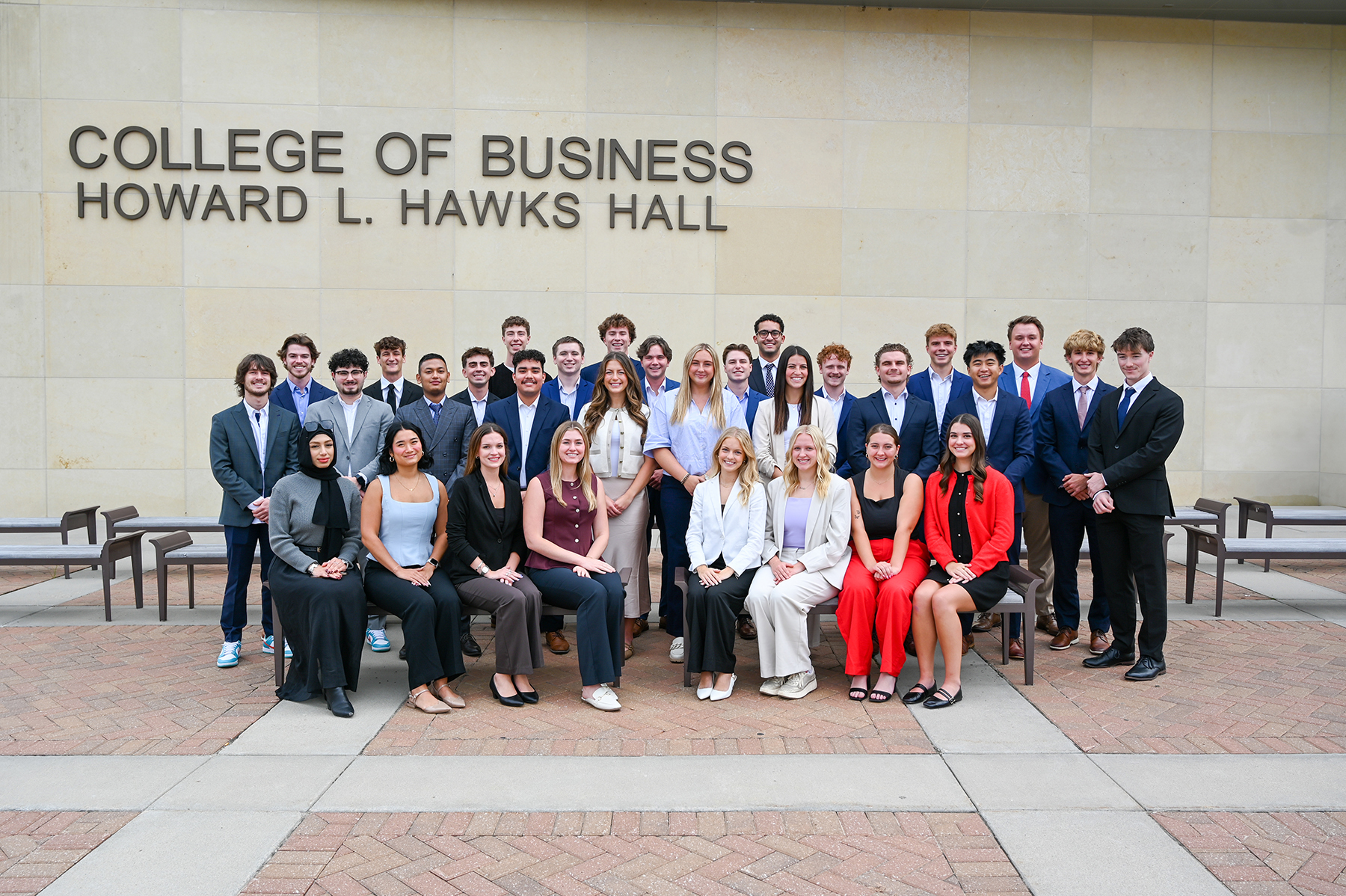 Thirty-one students — all members of the 10th cohort of the Clifton Builders Program at the University of Nebraska–Lincoln — pose for an outdoor photograph in formal attire on the west side of Howard L. Hawks Hall.