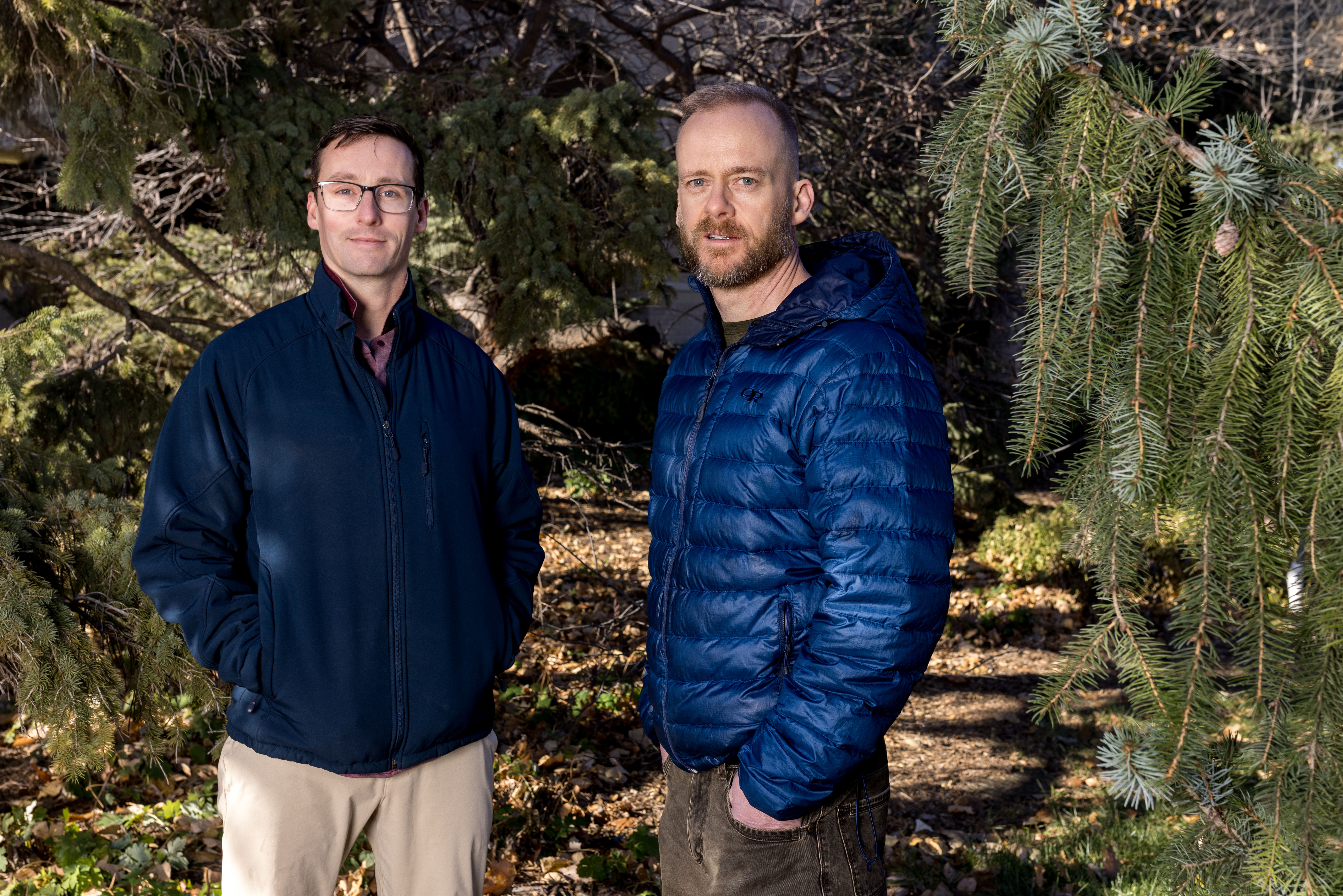 Kyle Dougherty and John Benson stand among trees in winter gear.
