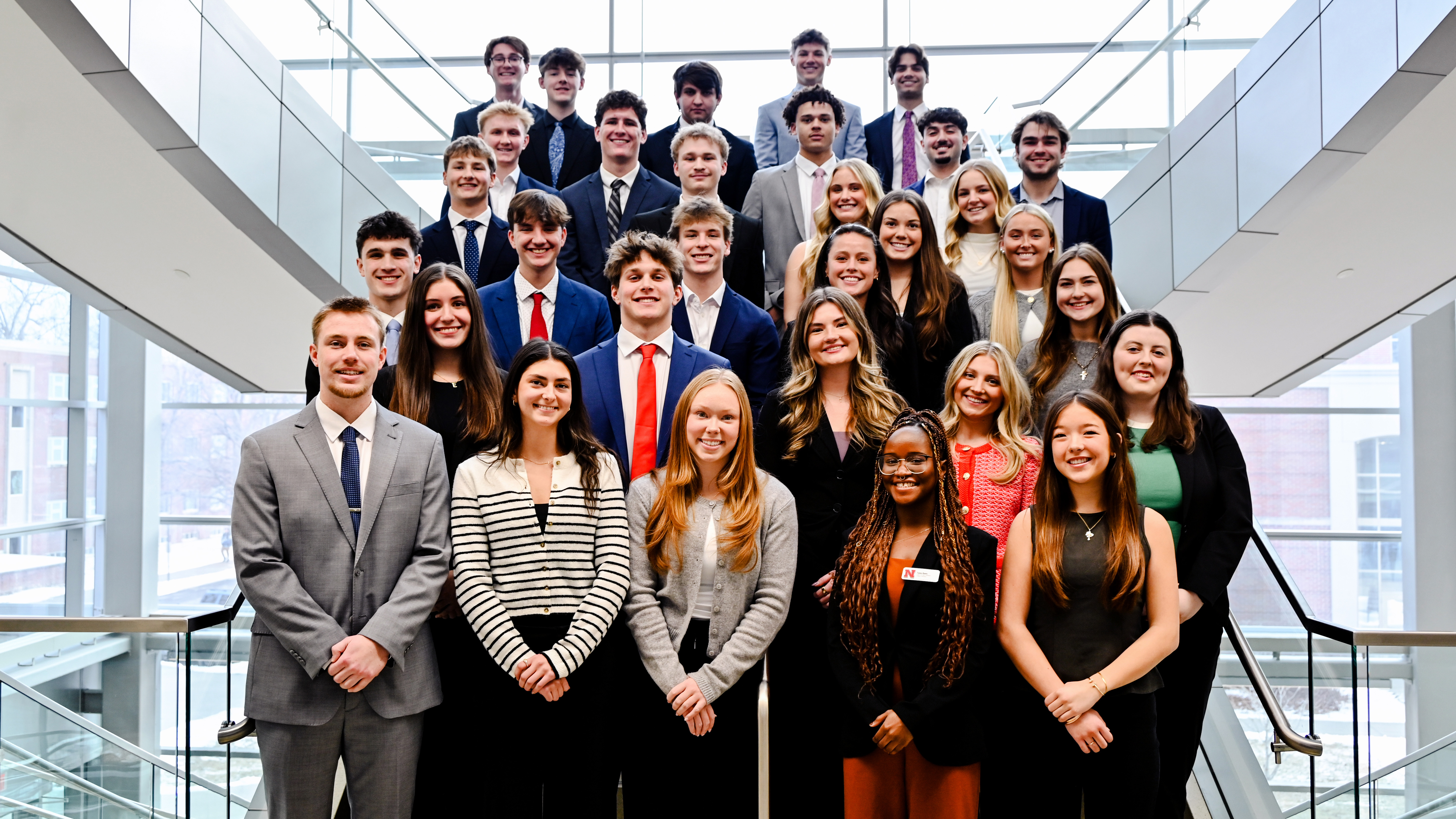 A group of about 30 University of Nebraska-Lincoln students in formal attire pose on a staircase in Howard L. Hawks Hall.