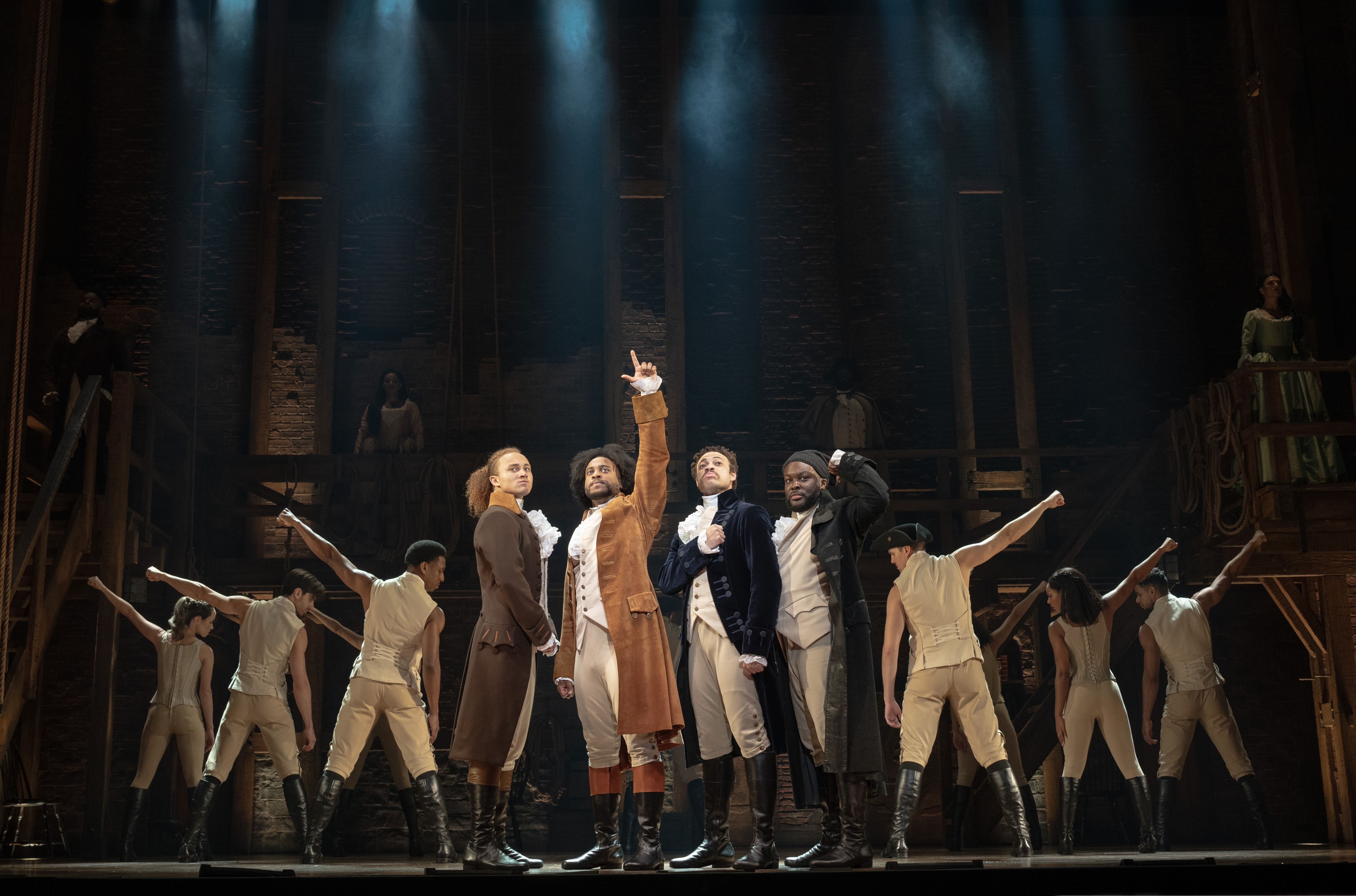 Four principal actors in Colonial-era costumes stand center stage with other cast members posing behind them in this publicity photo for "Hamilton."