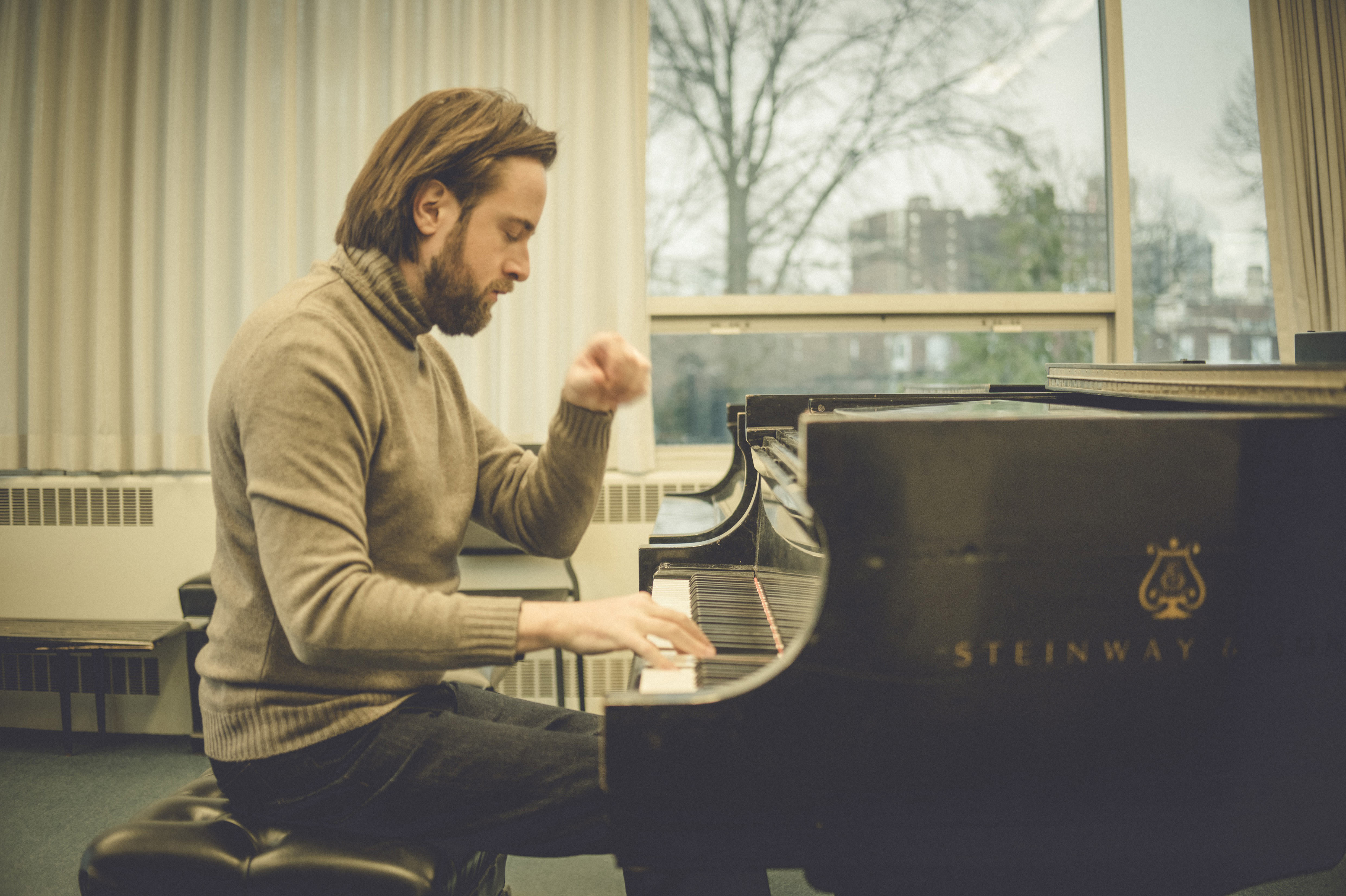 Daniil Trifonov, wearing a brown turtleneck and black jeans, plays a piano.
