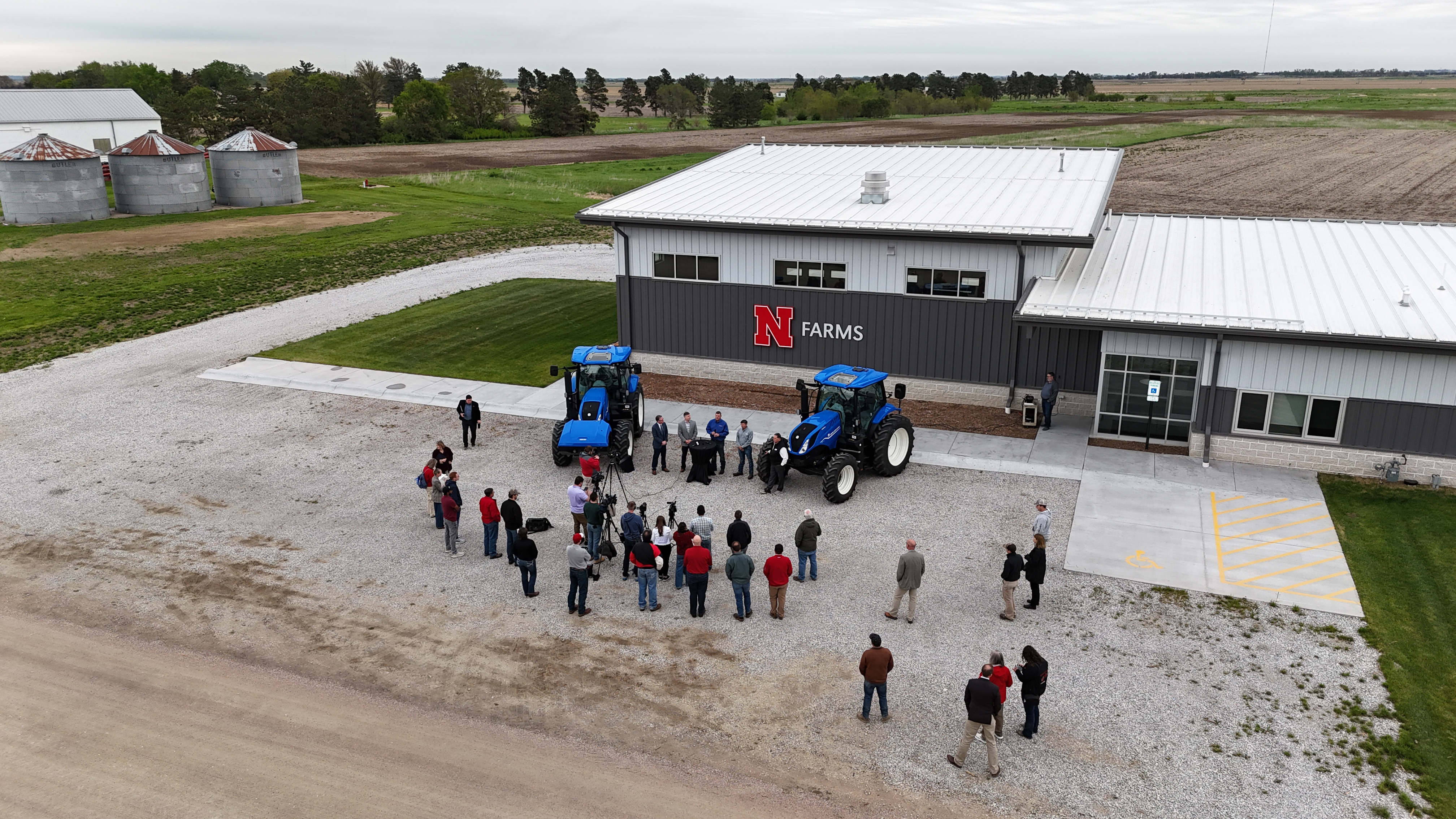 More than a dozen people gather around two New Holland methane-powered tractors outside the NFarms facility at the Eastern Nebraska Research, Extension and Education Center.