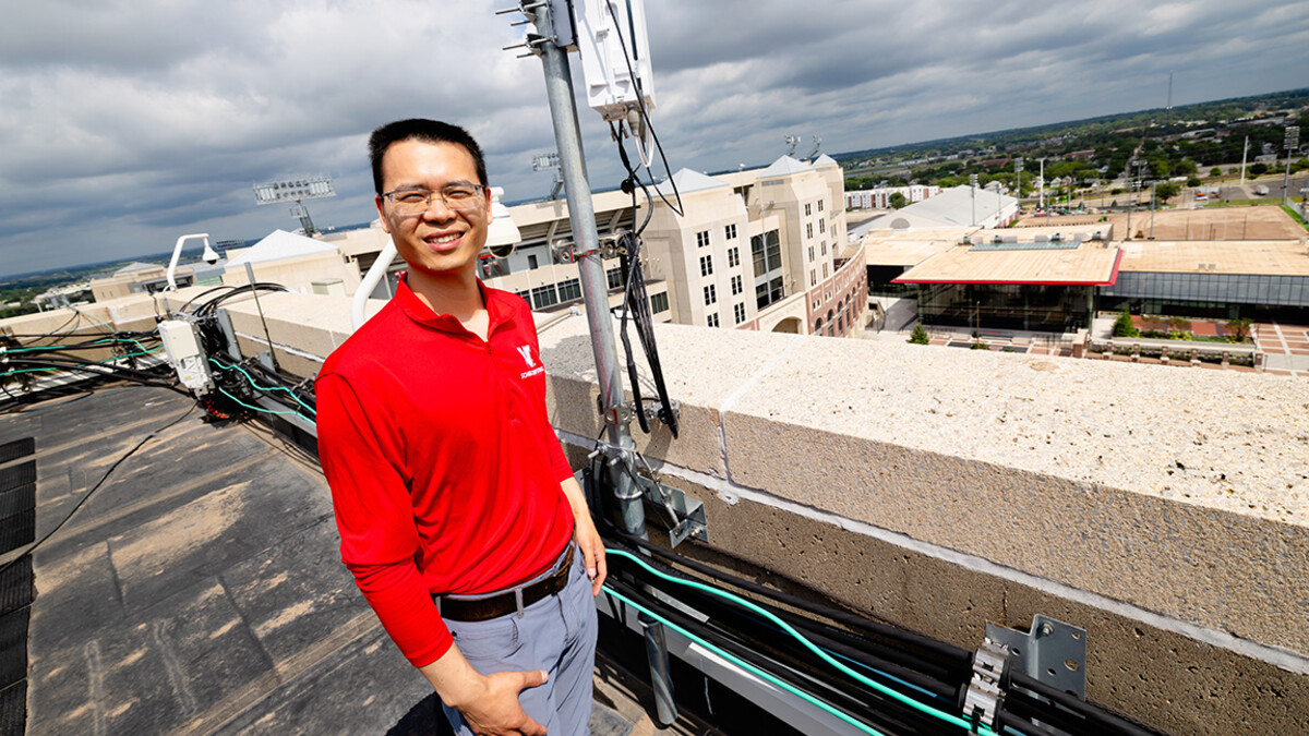 Qiang Liu, assistant professor in the School of Computing, stands next to one of the Husker-Net 5G amplifiers topping the roof of Oldfather Hall. Husker-Net is the University of Nebraska–Lincoln's private 5G network, and one of Liu's research focuses.