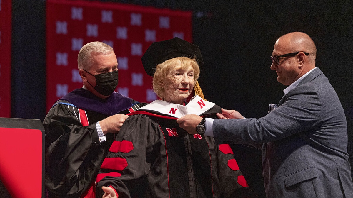 Leta Powell Drake, local television pioneer and Husker alumna, is hooded by University of Nebraska Regent Tim Clare (left) and her son, Aaron (right), during the University of Nebraska–Lincoln’s undergraduate commencement ceremony Aug. 14 at Pinnacle Bank Arena. The university presented Drake with an honorary Doctor of Humane Letters during the ceremony.