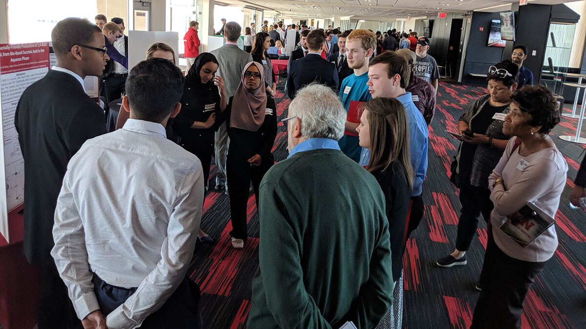 People standing around student booth at previous Senior Design Showcase