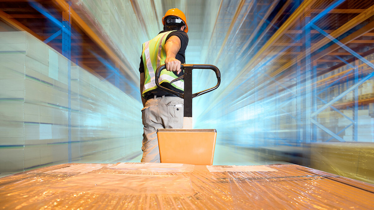 Man with orange helmet and yellow vest pulls palette of boxes