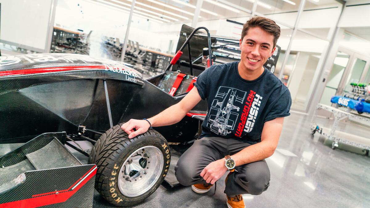 Nick Gauger, a senior mechanical engineering major, wears a Husker Motorsports T-shirt as he poses next to a black-and-red race car in the lower level of Kiewit Hall.