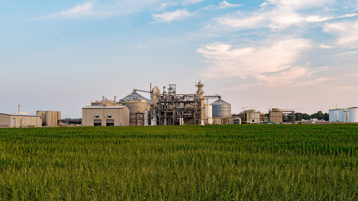 An ethanol plant is seen near a corn field on a partly cloudy day.