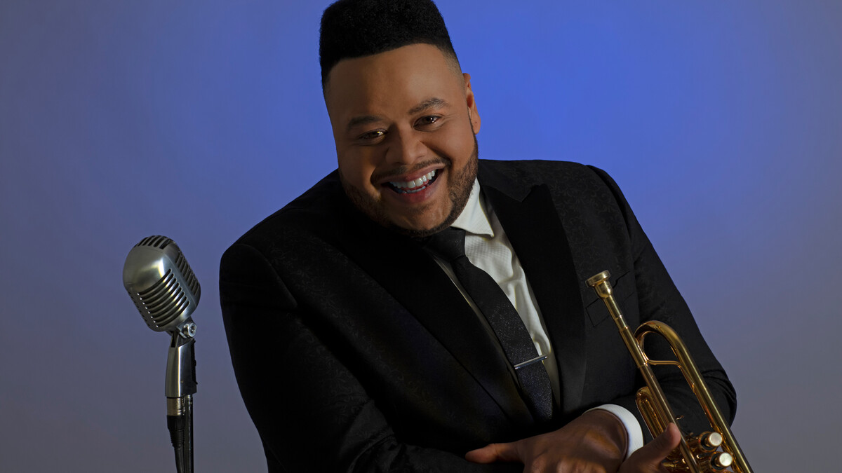 Color portrait of Jumaane Smith, holding a trumpet, next to a microphone.