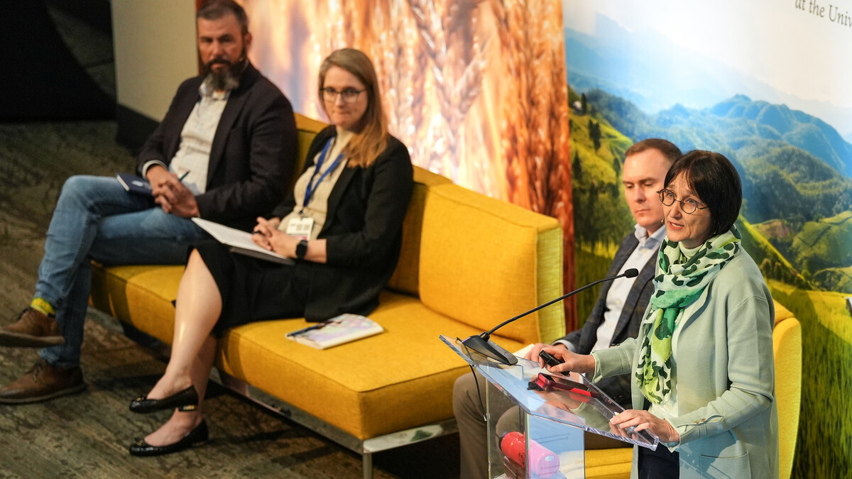 Claudia Ringler (right), director of natural resources and resilience at the International Food Policy Research Institute, delivers a keynote speech at a lectern as Brandon Hunnicutt (left), a Nebraska farmer and chairman of the Nebraska Corn Board; Abbie Raikes, director of UNMC’s Center for Global Health and Development (second from left); and Jesse Bell (second from right), director of water, climate and health at the Daugherty Water for Food Global Institute, sit and listen.