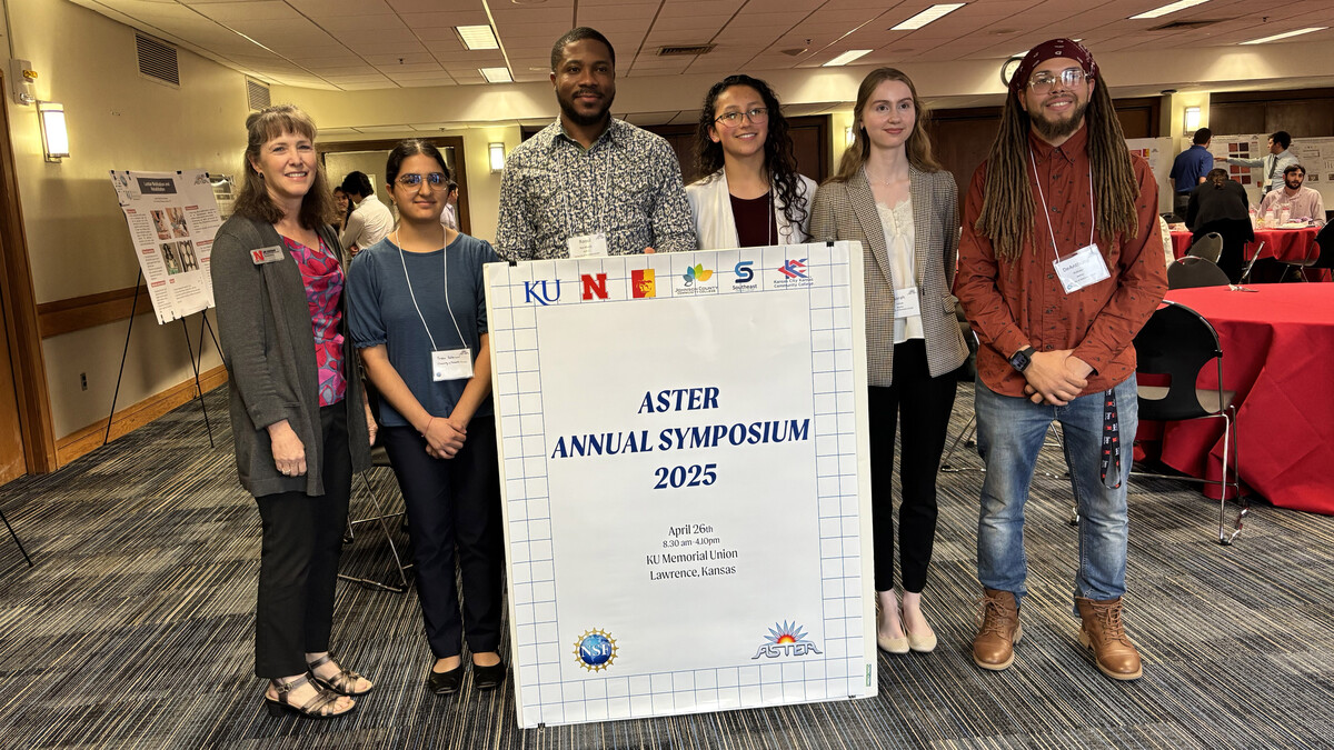 Amy Goodburn (left), senior associate vice chancellor, dean of undergraduate education and professor of English, stands alongside ASTER Symposium presenters (from left) Prisha Sabherwal, Raoul Patrick Nya Wandji, Danielle Barrera-Bojanski, Sarah Larson and DeAnthony Rothwell in a meeting room. They pose with a large white poster that reads "ASTER Annual Symposium 2025."