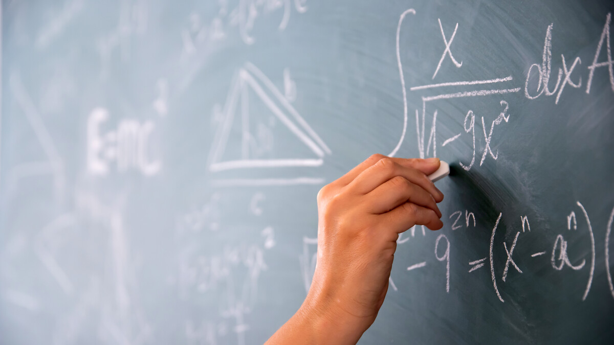A hand writes math equations on a chalkboard.