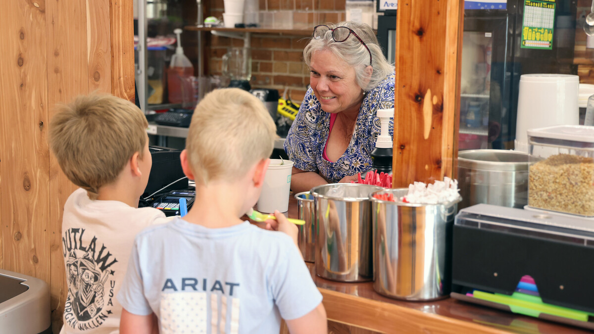 Two young boys buy ice cream from an older woman in a store.