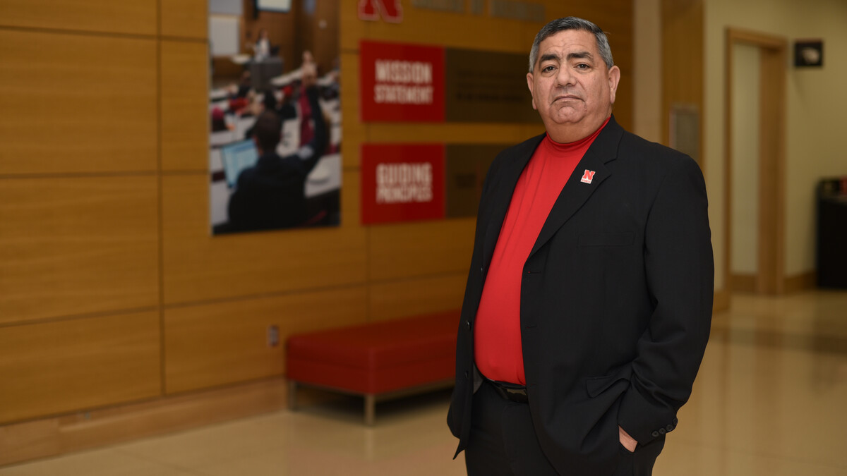 Rik Barrera, associate dean of operations and chief of staff in the University of Nebraska–Lincoln's College of Business, poses for a photo in a hallway of Howard L. Hawks Hall. He is wearing a black sport coat, red shirt and black dress pants.