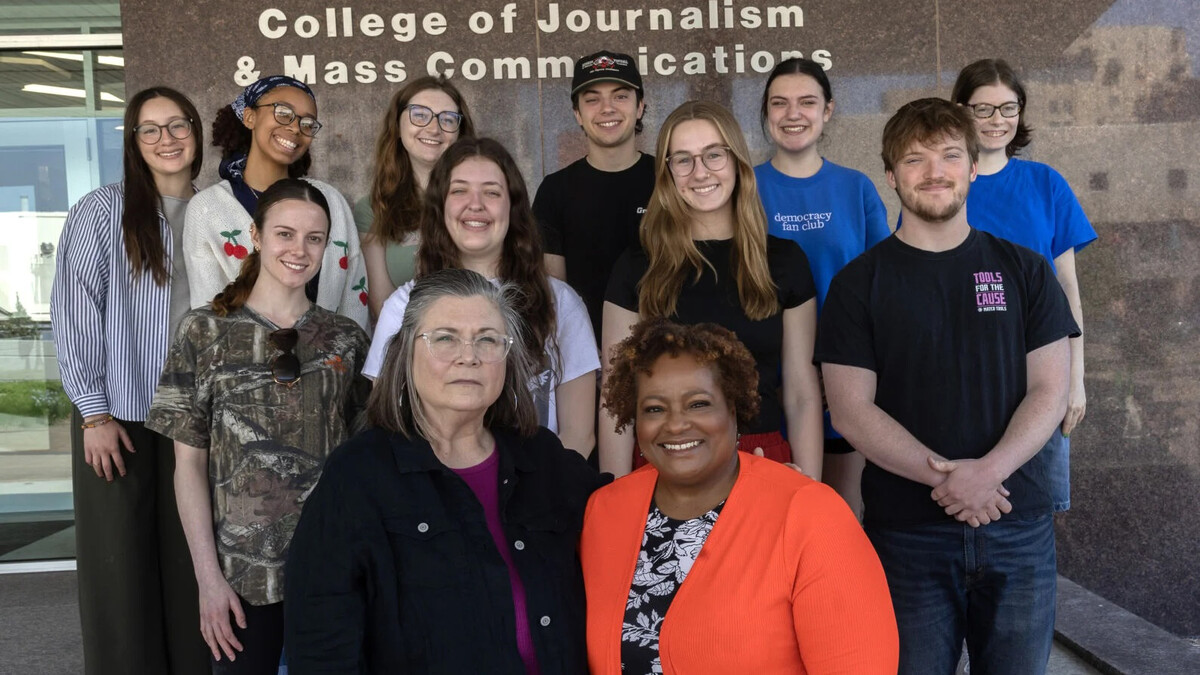 Ten Husker students — eight women and two men — and two female instructors pose for a group photo in front of Andersen Hall. The words "College of Journalism and Mass Communications" can be seen on the exterior wall.