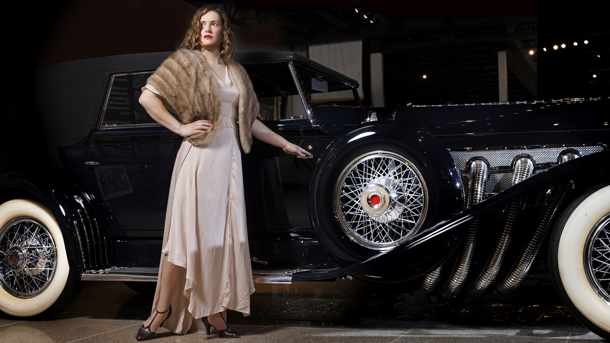 Anna Kuhlman evokes Hollywood glamour in this long 30s-style gown features bias cut panels and flowing sleeves in a soft pink. Paired with a vintage fur stole and T-strap heels.She poses next to a 1930 Duesenberg Model J at the Speedway Motors Museum of Speed. Kuhlman, who received her masters degree in May, researched fashion in the 1930s both in film and what was available in Nebraska.