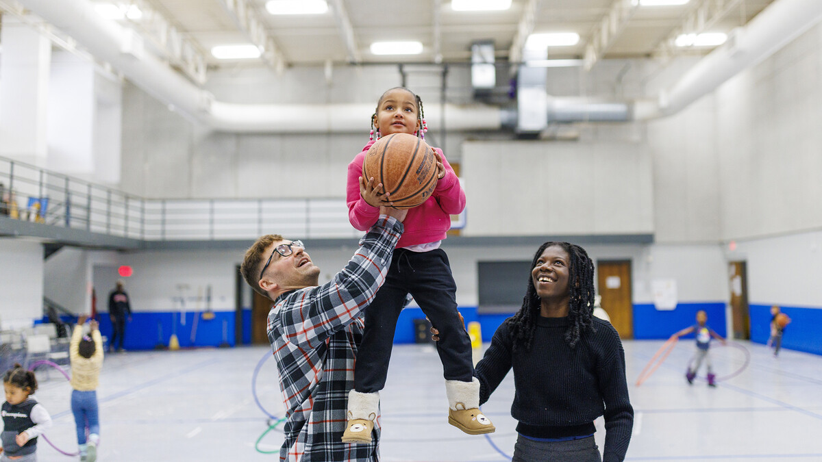 Ben Bentzinger, a senior in criminal justice, and Francisca Lawson Tettevie  a graduate student with CYAF, help Journey shoot a basket at the Malone Center.