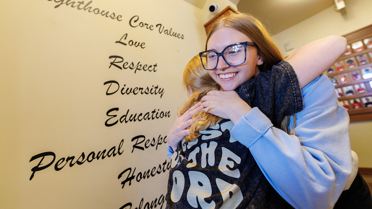 Two people hug in front of a wall with Lighthouse's core values.