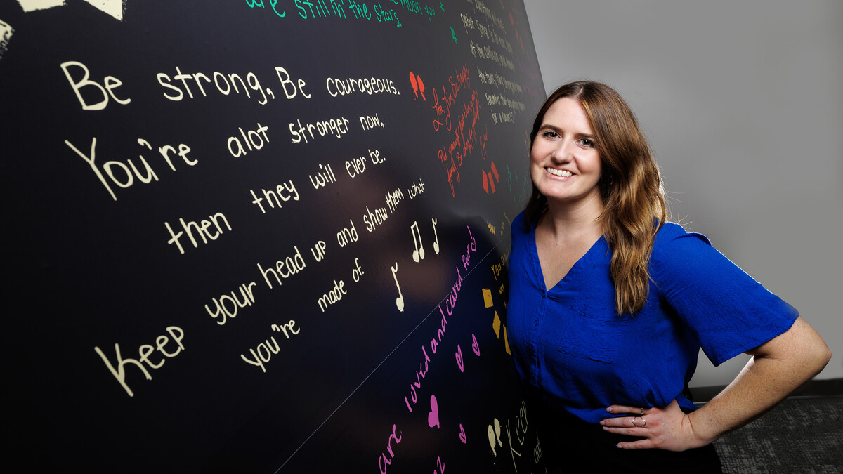 Gina May, Project SAFE clinical coordinator and graduate student, stands next to a wall containing inspirational messages inside the BraveBe Child Advocacy Center written by adolescent and teenaged clients.