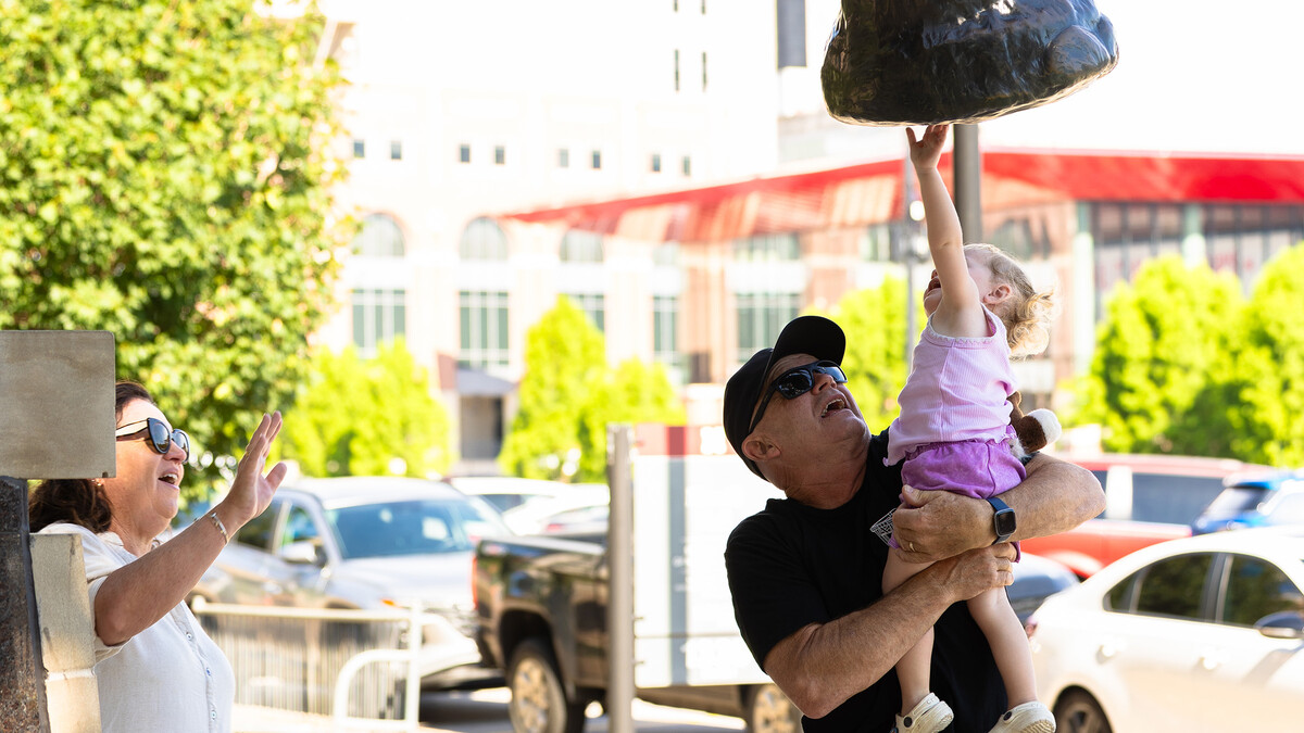 Greg Ferderer lifts his two-year-old granddaughter, Lexi, up to to Archie, the bronze mammoth statue in front of Morrill Hall. 