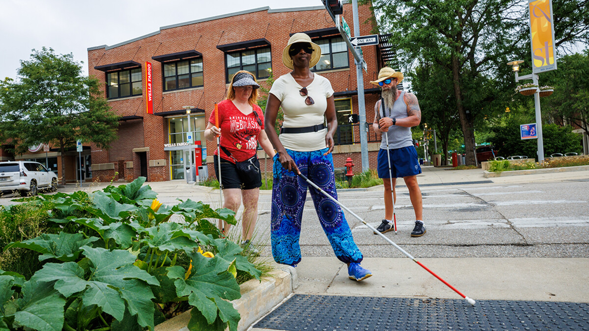 Sharon Cherono navigates around landscaping in downtown Lincoln using her long cane during an orientation and mobility course in the Department of Special Education and Communication Disorders. Kerry Trent (left) and Bob Lee walk behind Cherono.