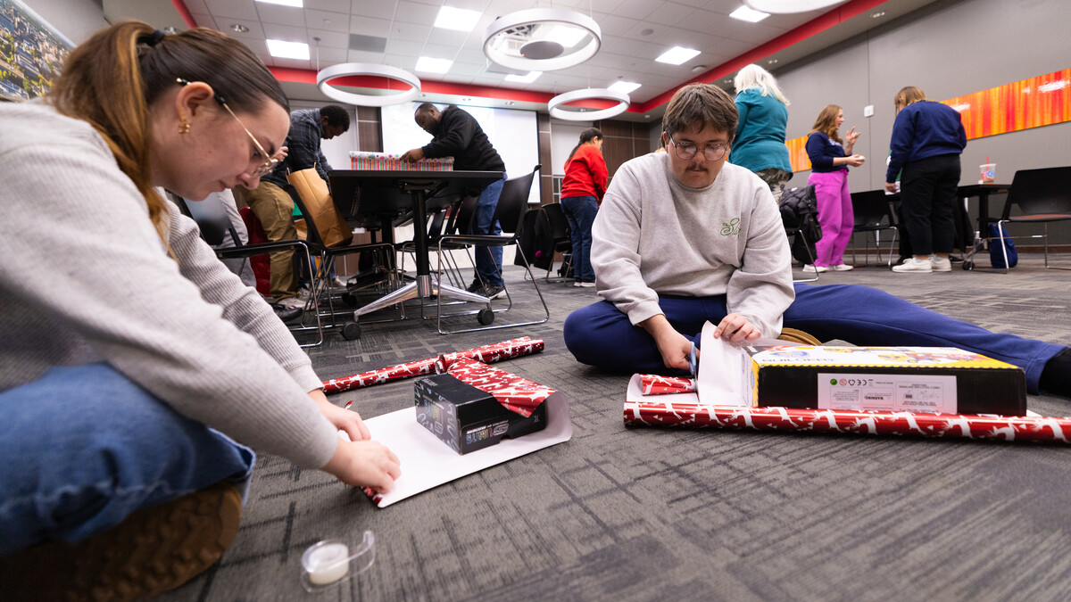 Two people sit on the floor and wrap gifts.
