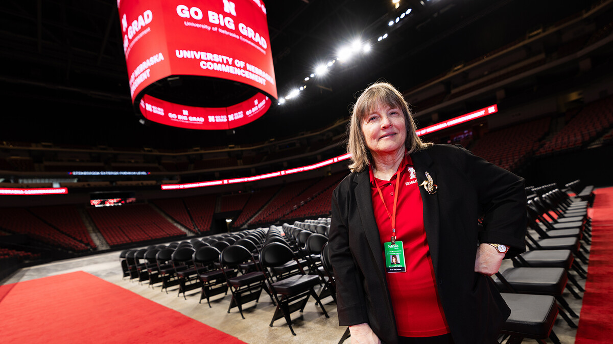Eva Bachman, director of graduate student support and associate registrar, stands in Pinnacle Bank Arena as crews set up for the graduate commencement ceremony on May 7. For 20 years, Bachman has worked behind the scenes to get graduate students successfully across the stage. She is wearing a brooch from her grandmother, who bought Bachman's textbooks and supported her academic journey.