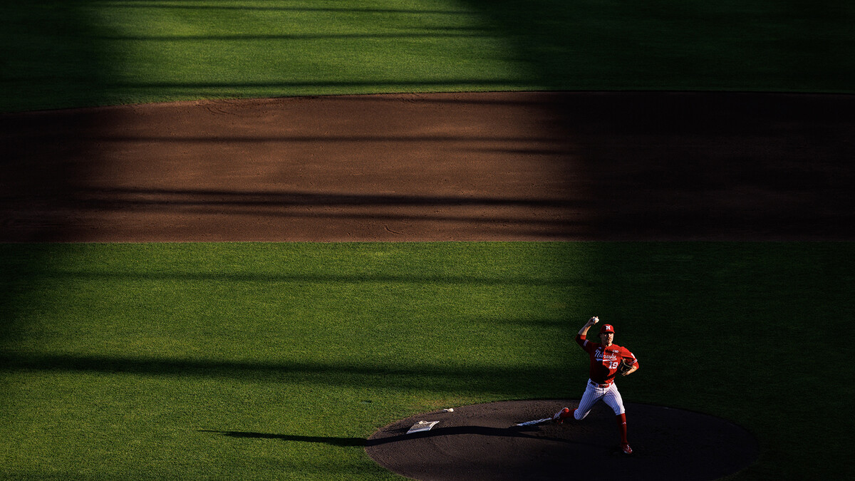 Nebraska pitcher Cooper Katskee throws a pitch during a game against the Creighton Bluejays at Charles Schwab Field Omaha as a beam of afternoon sunlight shines across the mound.