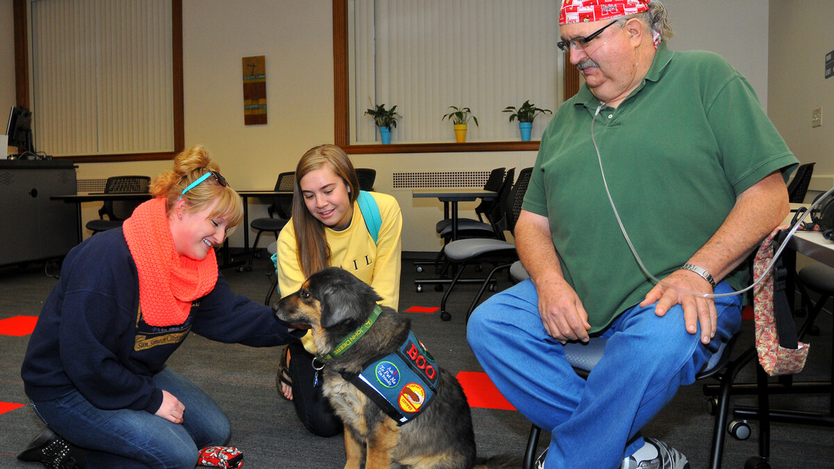 UNL students (from left) Lauren Martin and Laura Kowalski pet Boo, a Healing Hearts Therapy Dog, in Love Library on Oct. 15. Boo is a therapy and service dog owned by Gary Royal (right).