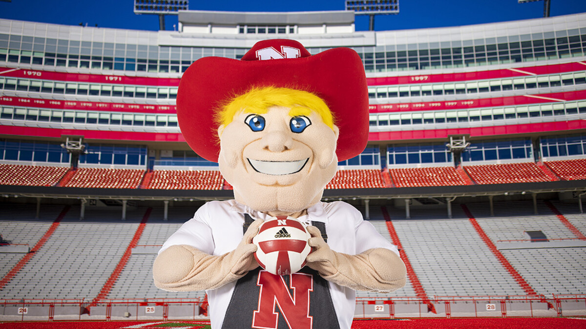 Herbie Husker stands in Memorial Stadium holding a volleyball.