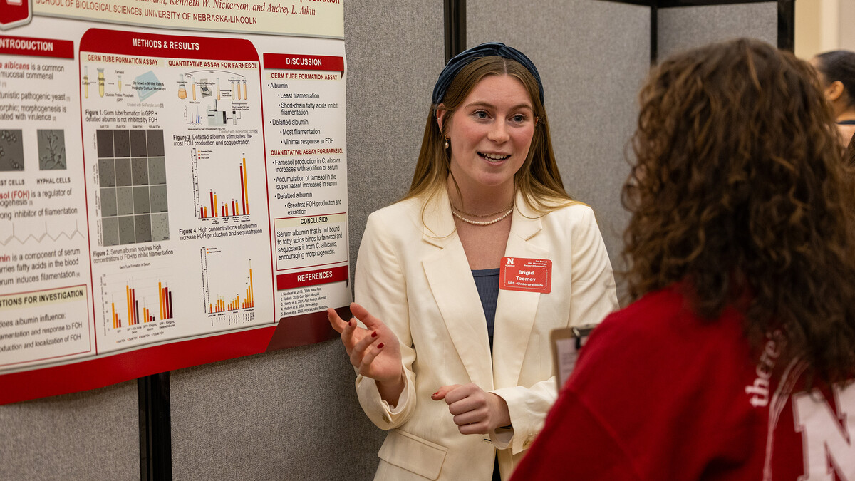 Undergraduate Brigid Toomey discusses her presentation, "The role of serum albumin in filamentation and farnesol sequestration," to a poster judge at the 2023 symposium.