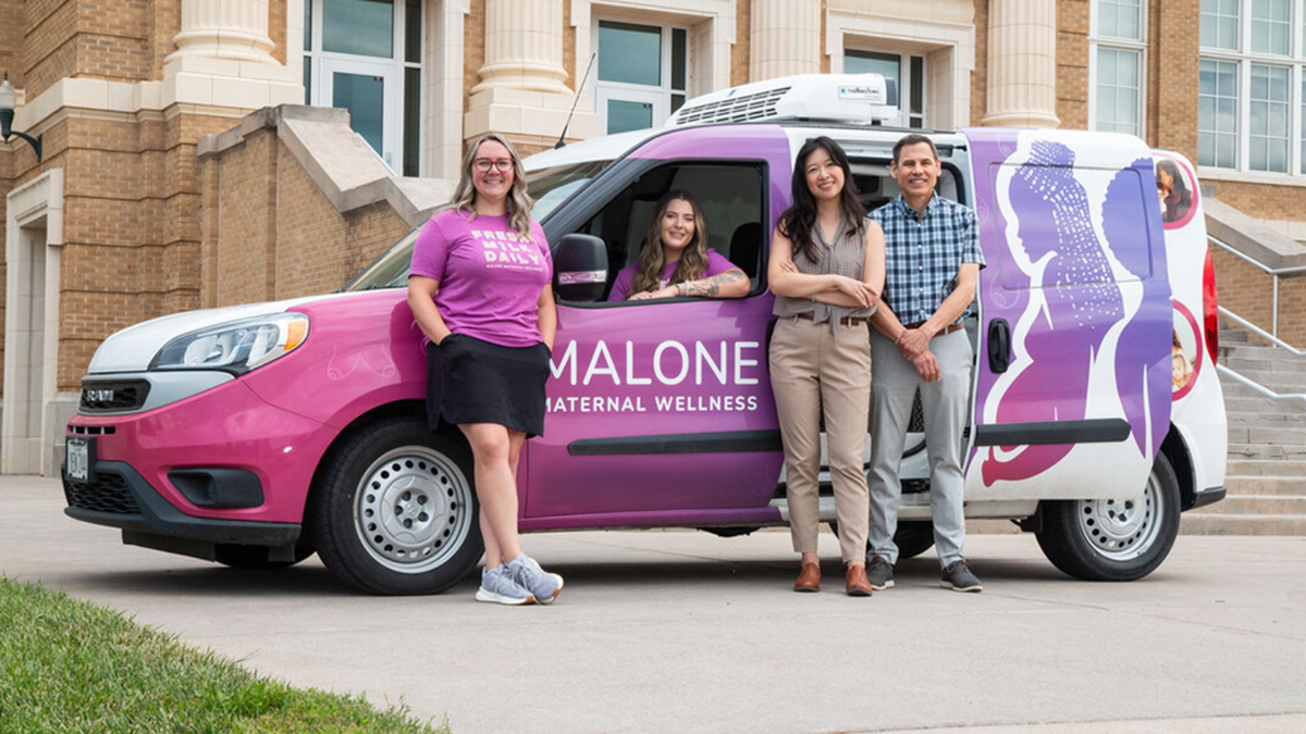 three people standing by the Malone Maternal Wellness car with a driver inside.