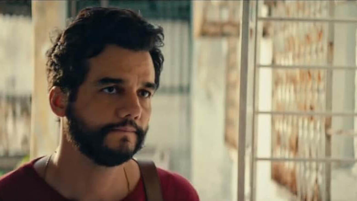 A brunette man with a beard stands in a red shirt.