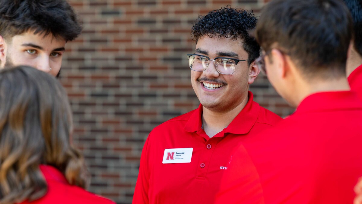 Leonardo Luna-Duran wears glasses and red collared tee shirt while chatting with fellow New Student Enrollment leaders.