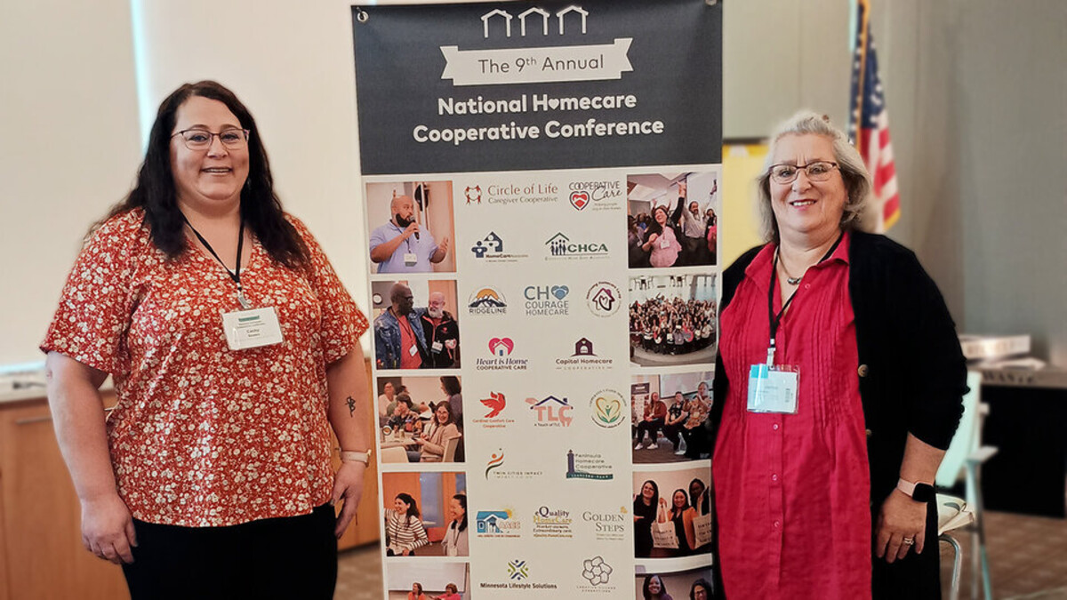 Two women stand on either said of a display at a conference.
