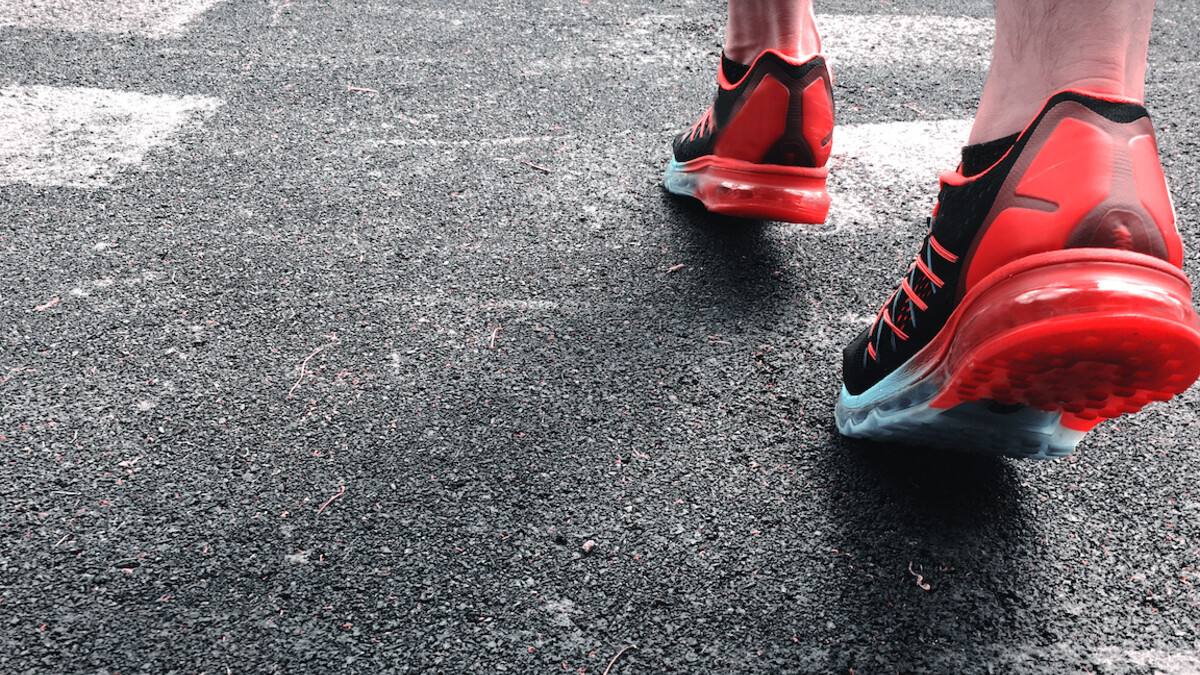 A person wearing red tennis shoes walking on concrete pavement