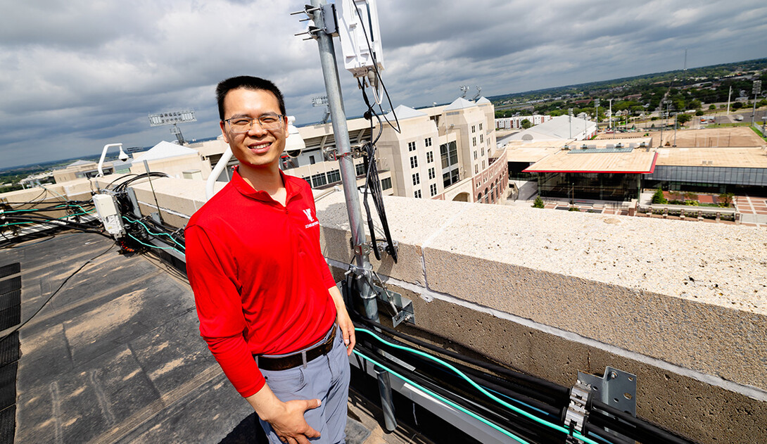 Qiang Liu, assistant professor in the School of Computing, stands next to one of the Husker-Net 5G amplifiers topping the roof of Oldfather Hall. Husker-Net is the University of Nebraska–Lincoln's private 5G network, and one of Liu's research focuses.