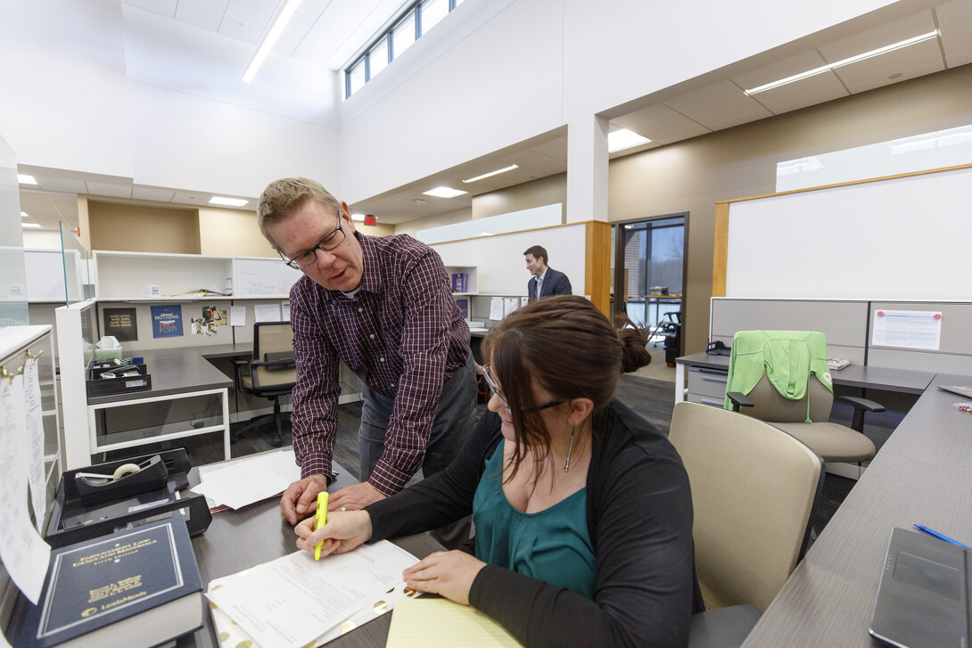 Professor Kevin Ruser and third-year law student Kelsey Heino review a case in the new workspaces of the Marvin and Virginia Schmid Clinic Building. Professor Ryan Sullivan is in the background.