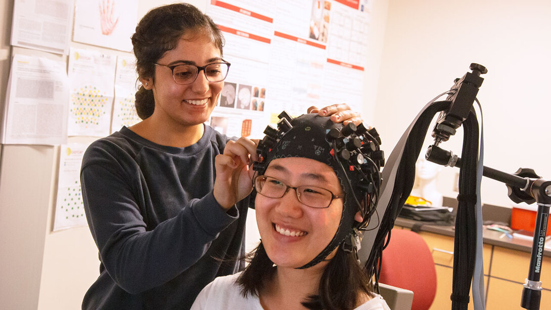 From left, student worker Randa Ismail adjusts an fNIRS cap on Grace Oh.