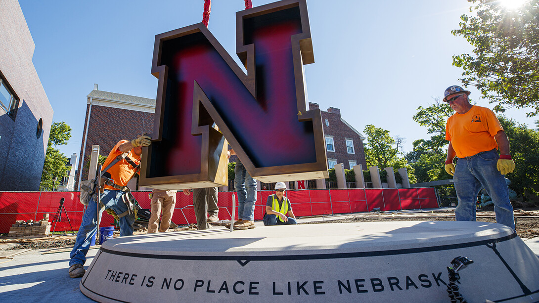 Artist Matthew Placzek (in white hard hat) watches as the new stainless steel N for the centerpiece of the Alumni Association's remodeled Holling Garden is lowered into place. The statue was positioned by a crane on June 24. 