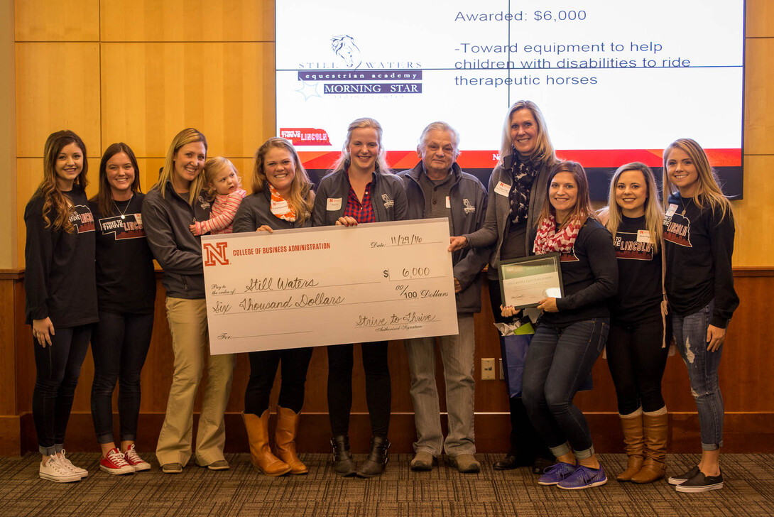 Leading People and Project Management class members present a $6,000 check to Still Waters Equestrian Academy. Pictured (from left) are students Haley Schepers and Megan Dennis, equestrian academy representatives Laura Stueck holding daughter Kennedy Stueck, Gracia Huenefeld, Tori Lee, Arnie Cole and Char Cole and students Gabby Knoble, Demi Patsios and Cami Kopetka.