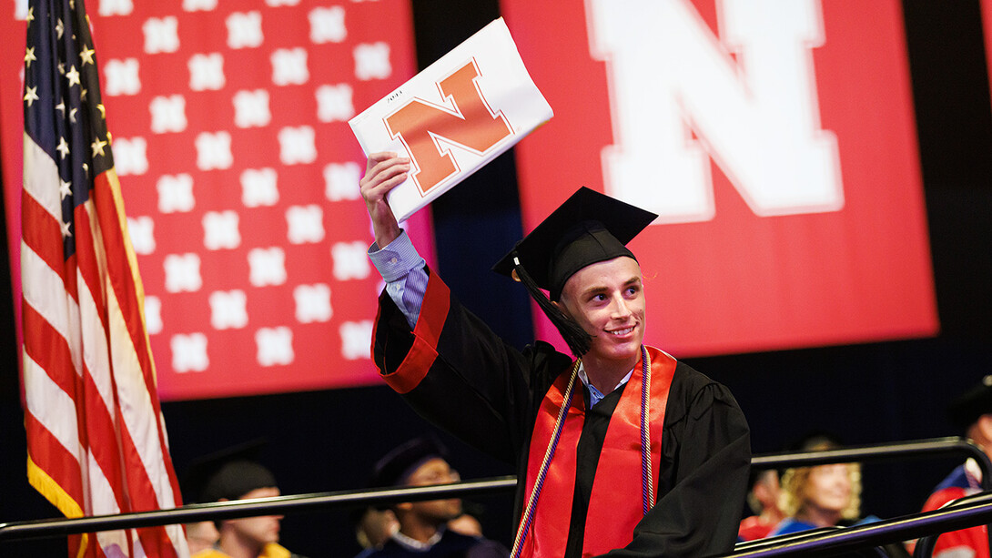 Joseph Rozek, dressed in graduation attire, raises his newly earned degree to family and friends. He earned a Bachelor of Science in Business Administration.