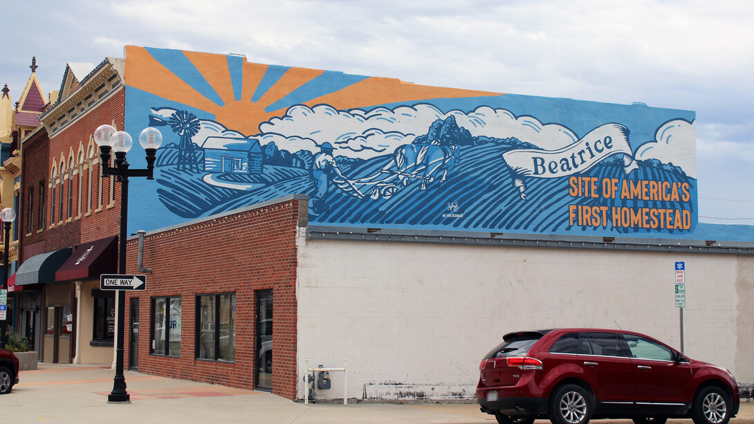 A mural of a farmer plowing a field with two cattle that reads "Beatrice: Site of America's First Homestead."