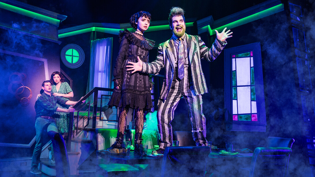 Beetlejuice, wearing a black-and-white striped suit, with Lydia and a young couple.