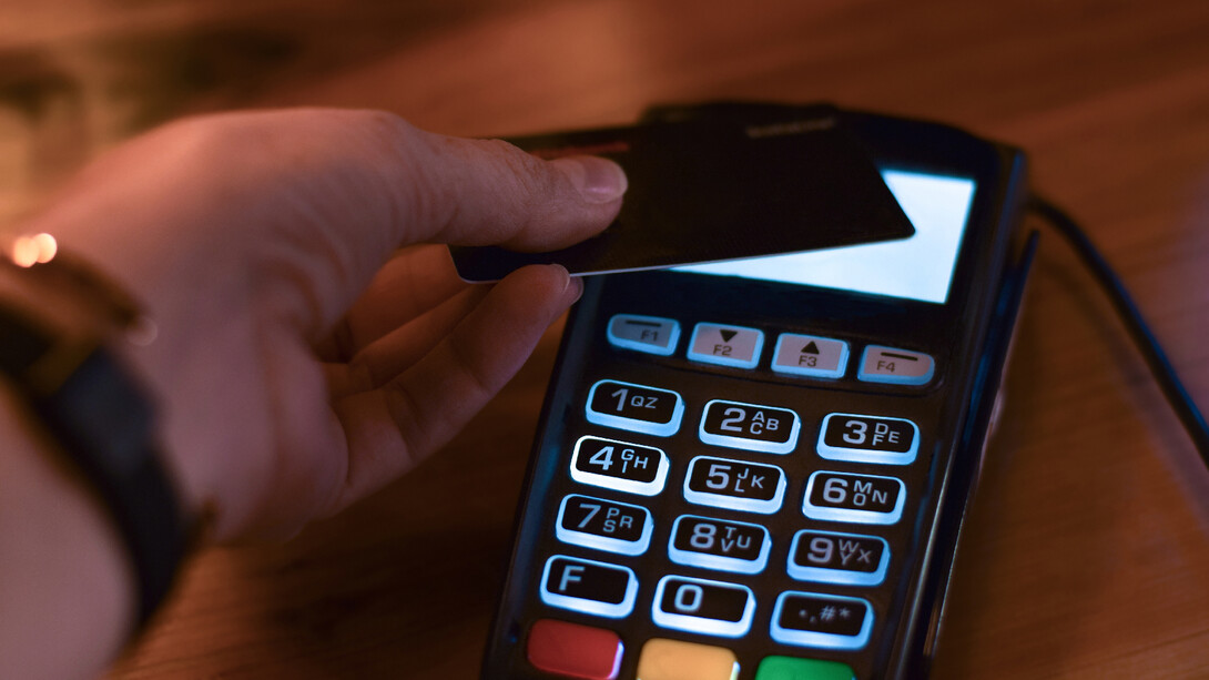 A hand taps a credit card on a reader.