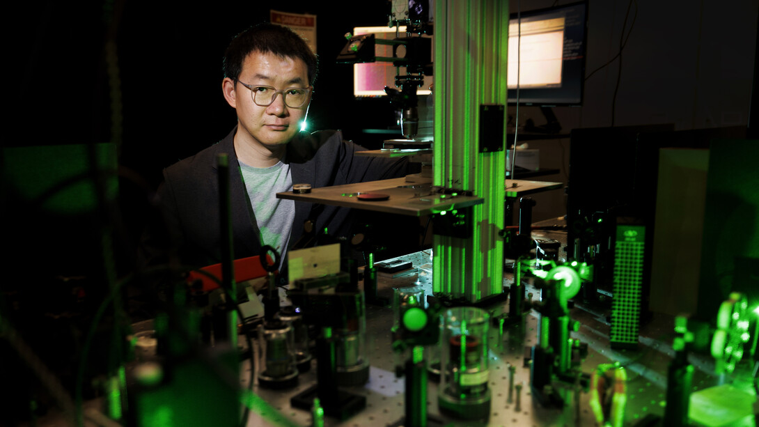 Yinsheng Guo stands over an array of instruments, glowing green in a dark room.